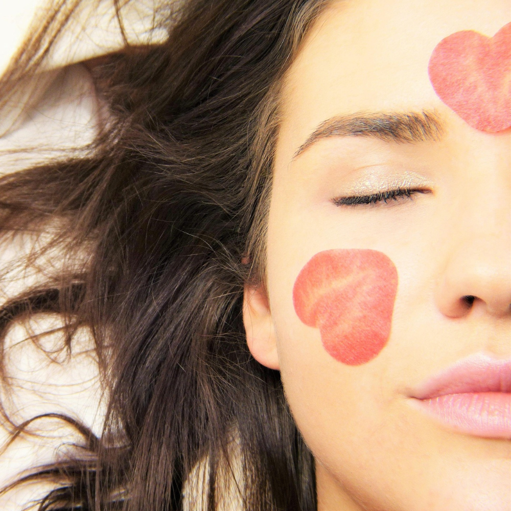 A women's face with hearts painted on her face.