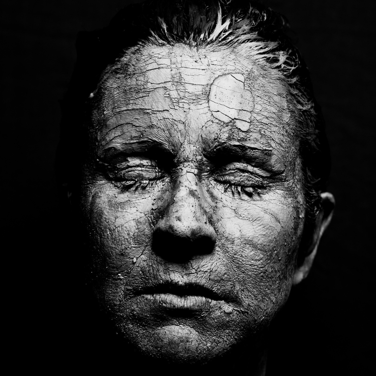 A face of a male with dried clay for natural facial treatment.
